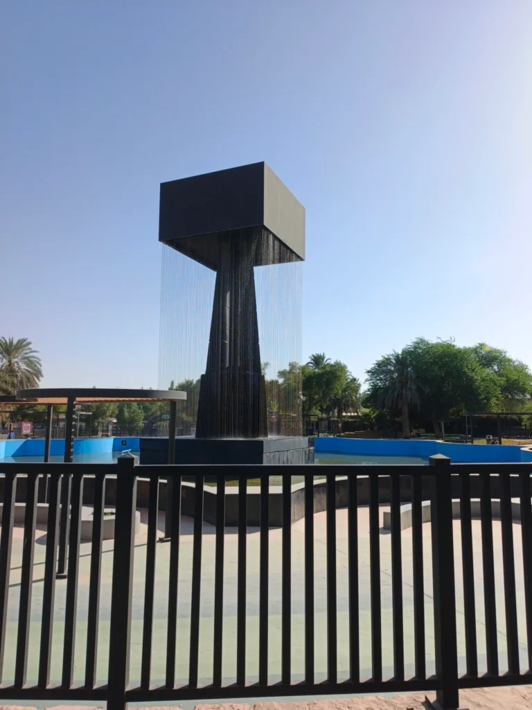 Modern black monolithic cube water fountain at Riyadh Zoo central plaza with water cascading into bright blue pool providing cooling effect